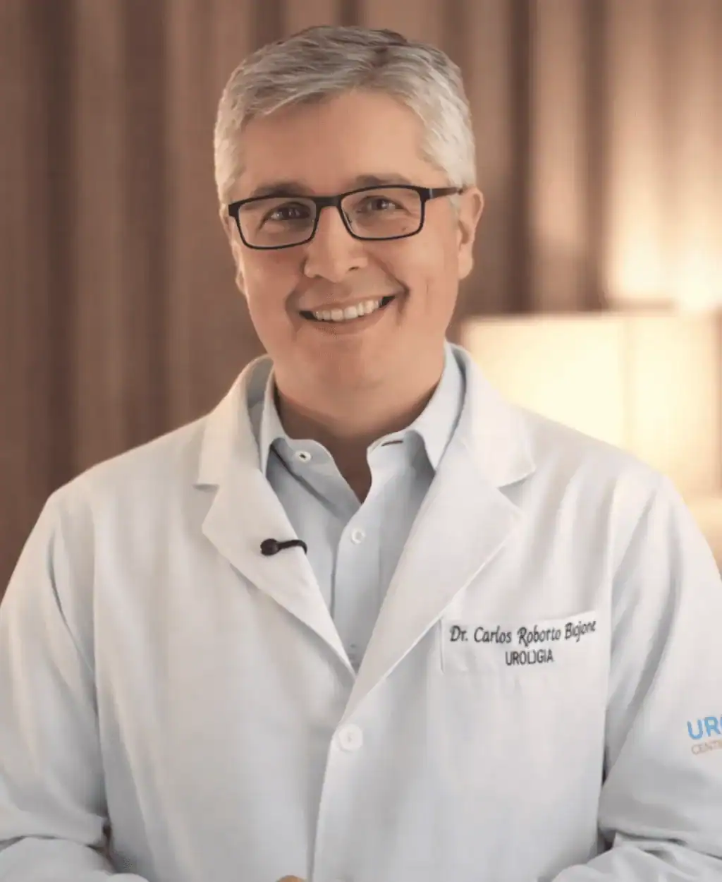 Dr. Carlos Biojone, urologista, sorrindo, vestindo jaleco branco bordado com seu nome e especialidade
